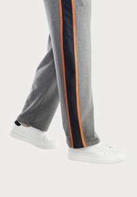 Graue Jogginghosen mit orangefarbenen und dunkelblauen Seitestreifen, ergänzt durch weiße Sneakers mit schwarzen Akzenten.