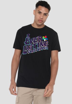 Young man wearing a black T-shirt with colorful "Everlasting Gobstopper" text and graphic, standing against a plain light gray background.