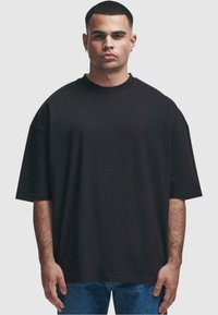 Černé oversized tričko z bavlny, kulatý výstřih, krátké rukávy, volný střih, hladká textilie, spárováno s modrými džíny.