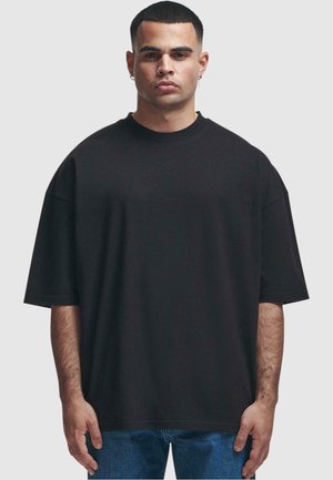 Černé oversized tričko z bavlny, kulatý výstřih, krátké rukávy, volný střih, hladká textilie, spárováno s modrými džíny.