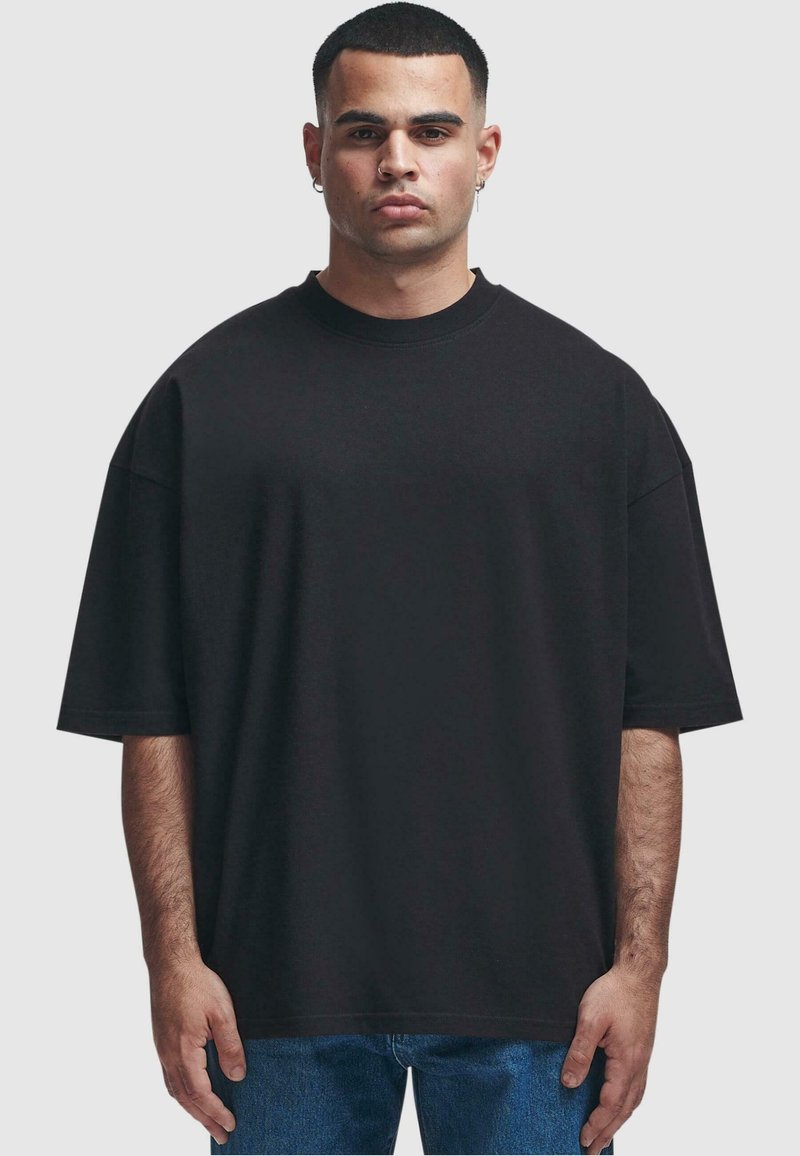 Černé oversized tričko z bavlny, kulatý výstřih, krátké rukávy, volný střih, hladká textilie, spárováno s modrými džíny.