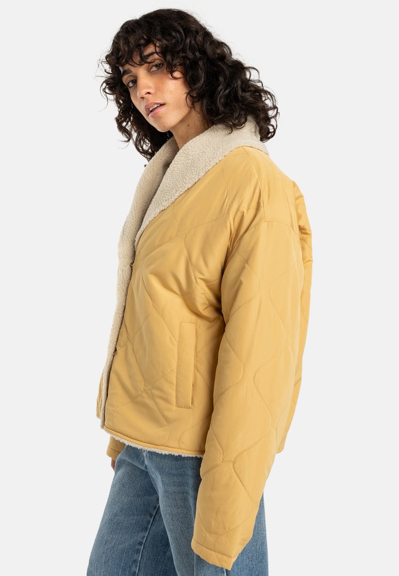 Gepolsterte gelbe Jacke mit einem flauschigen weißen Kragen, in kastiger Form, mit Seitentaschen und einer glatten Außenstruktur.