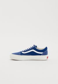 Baskets en toile bleue avec une bande en cuir blanc, des lacets blancs et une semelle en caoutchouc beige clair. Étiquette logo rouge sur le talon.