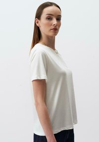 T-shirt a maniche corte, collo a giro in morbido tessuto bianco, vestibilità rilassata, texture liscia, con cuciture visibili e orlo leggermente arrotondato.