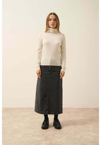 Krémový žebrovaný rolák, zkombinovaný s černou džínovou maxi sukni a masivními černými botami, stojící na světle texturované podlaze.