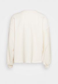 Pullover in felpa crema con vestibilità casual, spalle scese, maniche lunghe e scollatura rotonda. Texture morbida e minimalismo nei dettagli delle cuciture.