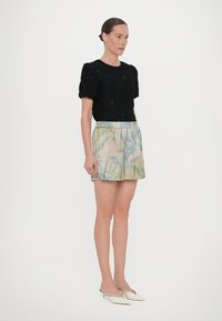 Zwarte getextureerde top met korte mouwen en pofmouwen, gecombineerd met lichte shorts met een groen-blauw bladerenpatroon. Witte hakken.