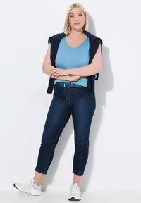 Vaaleansininen V-kauluspaita, jonka päällä tummansininen villapaita, tummat farkut, jotka ulottuvat nilkkoihin, ja valkoiset lenkkarit sinisillä yksityiskohdilla.