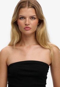 Top negro sin tirantes hecho de tela suave, con un diseño ajustado que realza el escote y los hombros. Líneas limpias y sencillas.