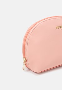 Astuccio cosmetico di colore pesca, con texture e forma curva, doppio zip e hardware dorato. Presenta il logo del marchio in rilievo.