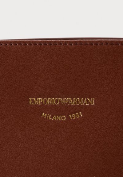 Καφέ υφή δέρματος με ανάγλυφο χρυσό κείμενο: "EMPORIO ARMANI" και "MILANO 1981." Ραμμένες άκρες και λεία επιφάνεια.