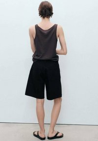Un débardeur noir, un short en denim noir et des sandales noires. La tenue est minimaliste, avec un design simple et sans motifs visibles.