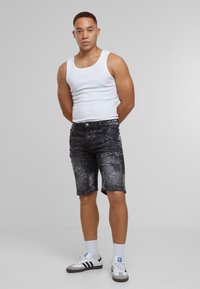 Černé džínové šortky s distressed detaily, vzorem nasprejování a pěti kapsami. Nosí se s bílým tílkem a neutrálními sportovními botami.