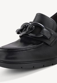 Mocassin en cuir noir avec un détail de grosse chaîne noire sur le dessus et une semelle basse en caoutchouc.