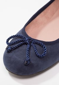 Marinblå mocka ballerina med rund tå, prydd med en texturerad, snurrad blå rosett och en mjuk rosa innersula. Slät ytteryta.