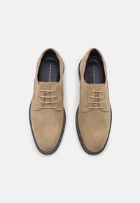 Chaussures à lacets en suède beige avec une texture lisse, bout arrondi et semelle extérieure en caoutchouc noir. Comprend sept œillets et un branding discret à l'intérieur.