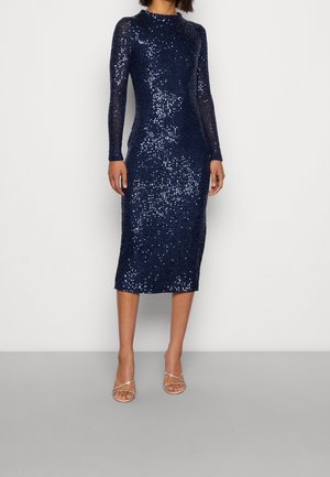 Robe en sequins bleu marine à manches longues, ajustée, de longueur genou. Présente un col rond et une texture lisse et brillante. Portée avec des chaussures à talons avec lanières.