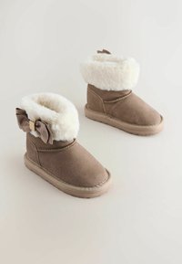 Bruine suède enkelboots met een witte faux fur zoom, een strikdetail aan één kant en een getextureerde rubberen zool voor grip.