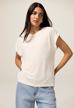 T-shirt blanc à manches courtes avec une coupe décontractée, un col rond et un tissu doux, associé à un jean en denim bleu clair avec des détails subtils.