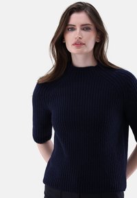 Navyblauer, gerippter Strickpullover mit kurzen Ärmeln und hohem Kragen, aus weichem Material gefertigt. Mit einer figurnahen Silhouette.