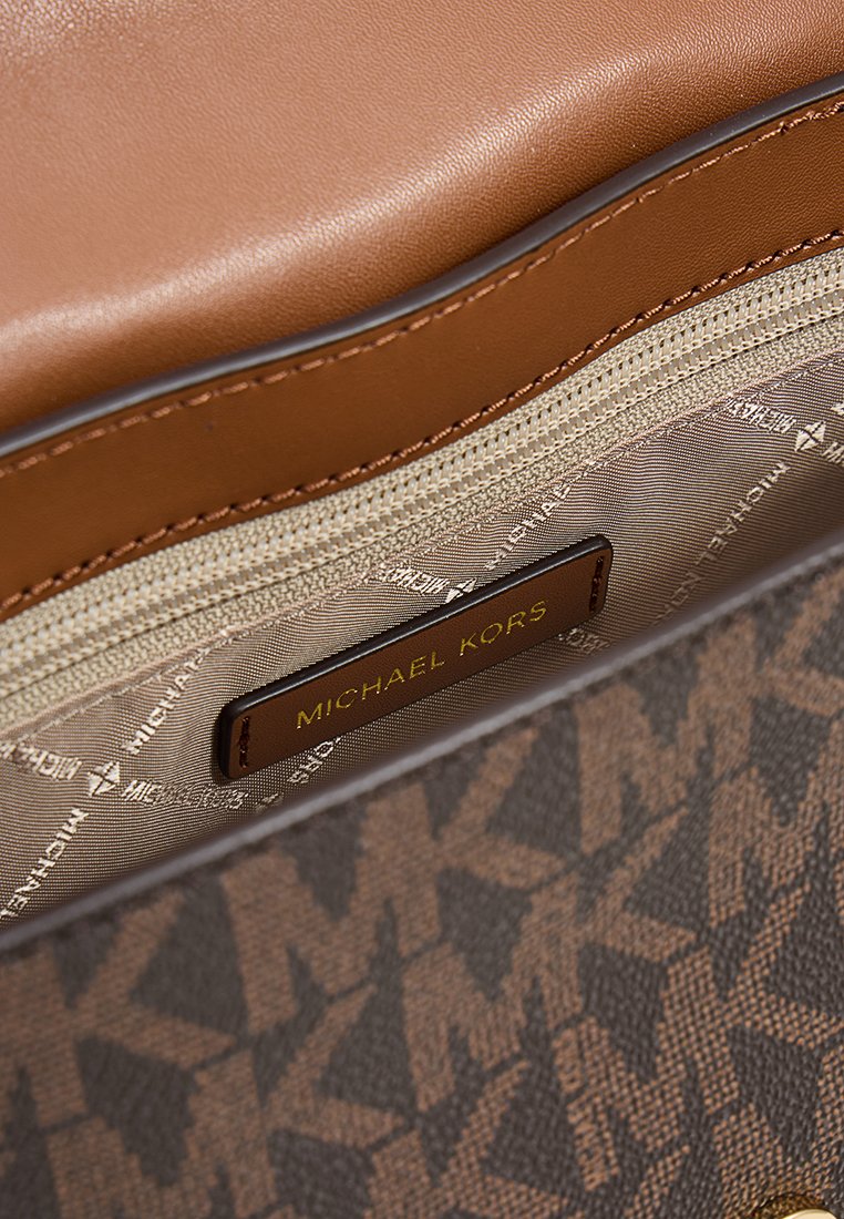 Innerraum einer braunen Ledertasche mit einem sandfarbenen Reißverschluss und beigem Futter, das ein sich wiederholendes "Michael Kors"-Muster zeigt. Goldenes Logo-Element sichtbar.