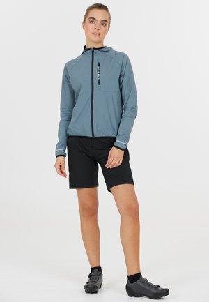 Lättviktsgrå jacka med huva och framfickor, kombinerad med svarta shorts. Svarta cykelskor fulländar looken.