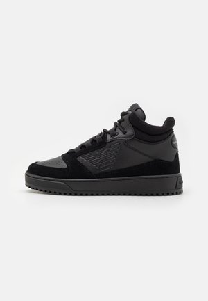 Baskets montantes noires en cuir texturé et panneaux en suède, fermeture à lacets et logo embossé sur le côté, sur fond blanc.