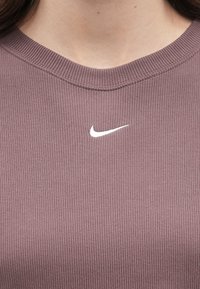 Κοντινό πλάνο από τον λαιμό μιας ριγέ μωβ μπλούζας με το λογότυπο Nike σε λευκό, το οποίο βρίσκεται κεντραρισμένο κάτω από τον γιακά.