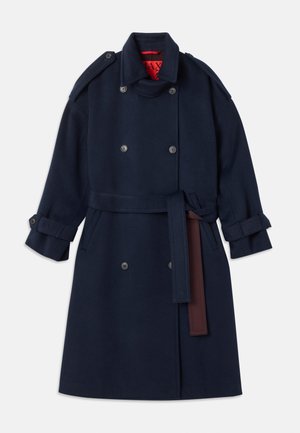 Manteau trench en laine bleu marine avec fermeture à double boutonnage, taille ceinturée, doté de grands revers et de pattes de poignet. Doublure intérieure rouge.
