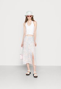 Top halter branco combinado com uma saia de padrão floral em tons pastel, apresentando uma fenda lateral. Os acessórios incluem um leve chapéu bucket e uma bolsa rosa.