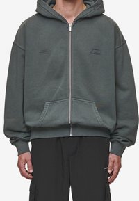 Felpa grigia con zip, dotata di una grande tasca frontale, polsini a costine e cappuccio. Presenta loghi ricamati in modo sottile, realizzata in morbido tessuto di cotone.