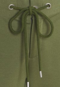 Felpa verde oliva con cappuccio, dotata di lacci in corda spessa, caratterizzata da occhielli in metallo argentato e una superficie liscia e testurizzata.