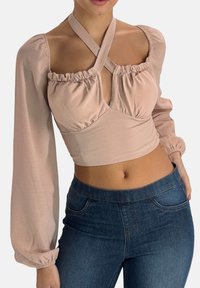 Blushfarbene, kurz geschnittene Bluse mit Puffärmeln, Rüschendetails und tiefem V-Ausschnitt, kombiniert mit dunkelblauen eng anliegenden Jeans.