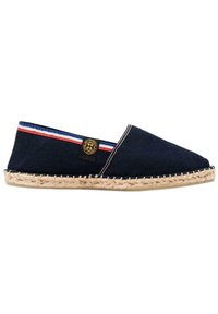 Espadrille en toile marine avec semelle en jute tressé, présentant un accent rayé rouge et blanc et un patch de logo de marque noir sur le côté.