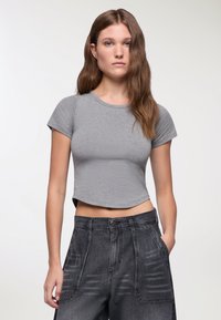 T-shirt grigio corto con scollatura rotonda e maniche corte. Tessuto morbido, aderente al torso. Abbinato a pantaloni in denim scuri a vita alta.