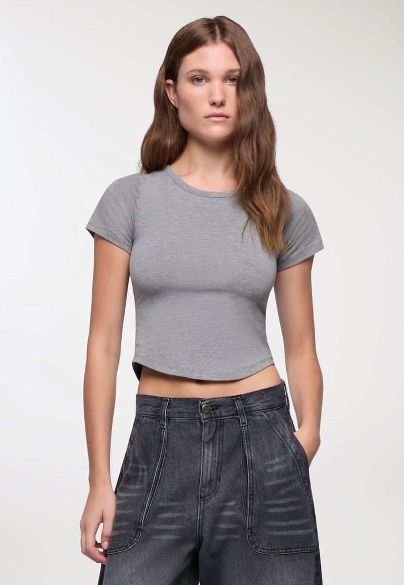 T-shirt grigio corto con scollatura rotonda e maniche corte. Tessuto morbido, aderente al torso. Abbinato a pantaloni in denim scuri a vita alta.