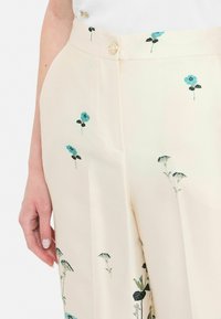 Pantaloni floreali crema con motivi blu e verdi, tessuto morbido, tasche laterali e chiusura con un solo bottone in vita.