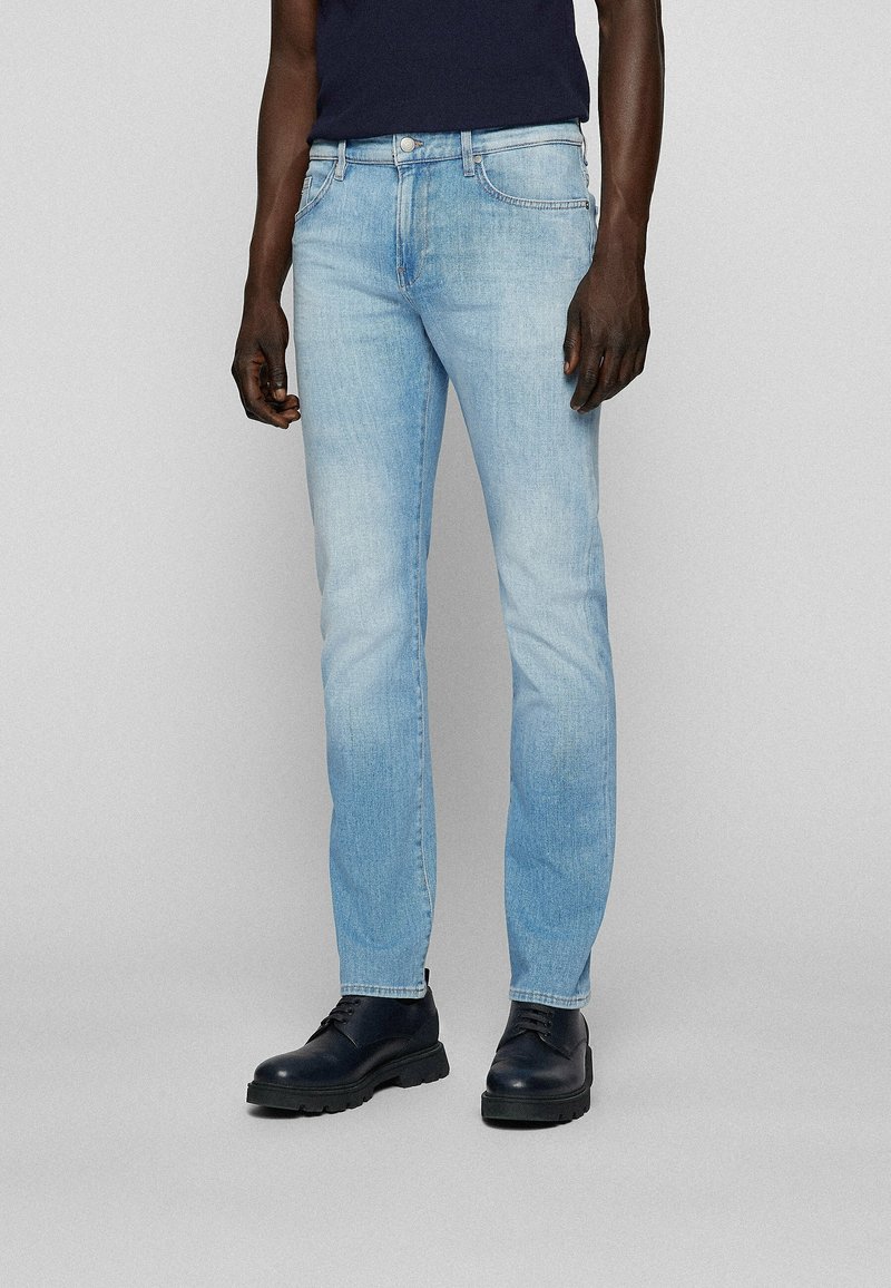 Jean en denim bleu clair avec une coupe droite, un léger délavage, un style cinq poches et des passants pour ceinture. Porté avec des bottes en cuir noir.