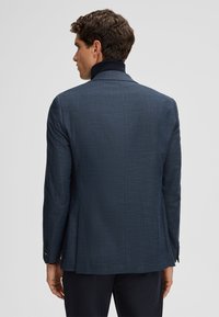 Navy textuur jack met een hoge kraag, enkele split en zwarte knopen. Beschikt over een getailleerde pasvorm en een subtiel patroon.