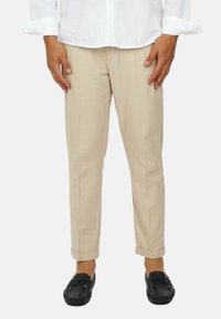 Pantaloni di cotone beige con taglio dritto, caratterizzati da una superficie liscia e orli arrotolati. Abbinati a scarpe mocassino nere.