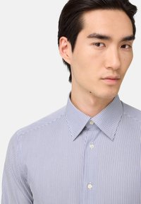 Prúžkovaná košeľa s límcom, ktorá má úzke modré a biele vertikálne pruhy a hladkú bavlnenú textúru.