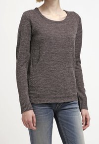 Brun texturerad tröja med rund halsringning, långa ärmar och ribbad nederkant, parat med ljusa denimjeans. Avslappnad och enkel design.