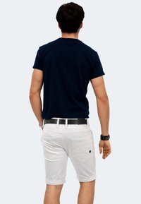 Navy blue short-sleeve t-shirt paired with white rolled-up shorts, black belt, and watch, viewed from the back. Minimalistic design.