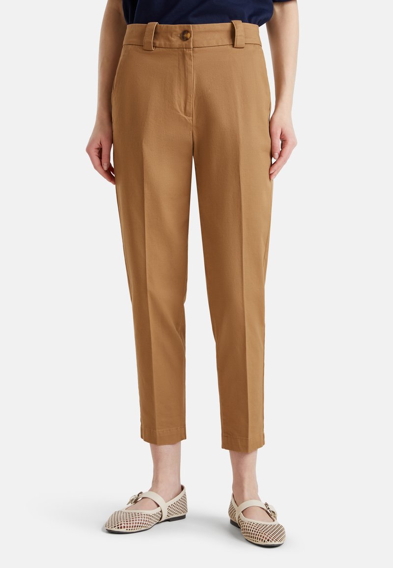 Kobieta w krótkich, beżowych spodniach i w beżowych, plecionych balerinach, stojąca z rękami swobodnie wzdłuż ciała na białym tle.