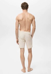 Beige linnedshorts med elastisk talje, baglomme og afslappet pasform, vist fra ryggen på en stående mandlig figur.