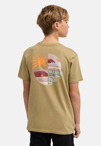 Khaki katoenen T-shirt met een kleurrijke afbeelding op de achterkant van een zon, golven en de tekst "BILLABONG FEELING FREE 73." Korte mouwen.