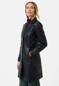 Black leather coat featuring a button front, pointed collar, and two side pockets. Smooth texture with a tailored fit and knee-length design.