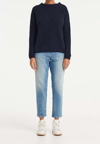 Granatowy sweter z prążkowanego dzianiny o okrągłym dekolcie, zestawiony z jasnoniebieskimi, zwężanymi jeansami oraz białymi trampkami za kostkę.