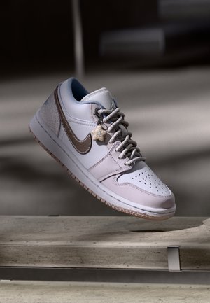 Baskets Nike gris clair avec une texture lisse, dotées d'un swoosh marron, d'un système de laçage et d'un charme en forme d'étoile sur les lacets.