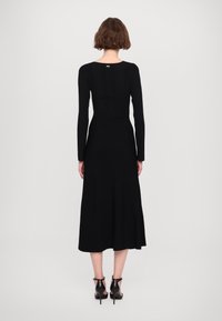 Abito lungo nero a maniche lunghe con corpetto aderente e gonna fluida. Realizzato in tessuto texturizzato, presenta uno scollo sul retro e un'etichetta del marchio sottile.